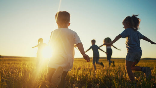 A group of children joyfully running through a grassy field during sunset
