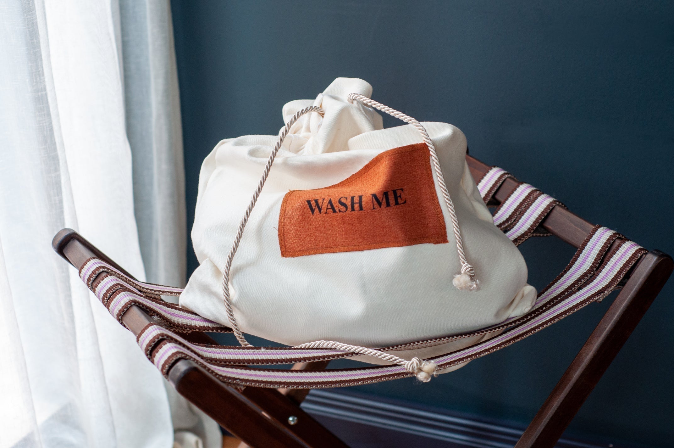 A white canvas bag with a "Wash Me" label, placed on a wooden folding stand, ready for cleaning.
