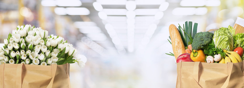 "Eco-friendly tote bags filled with fresh white tulips and a variety of groceries, including vegetables, fruits, and bread.