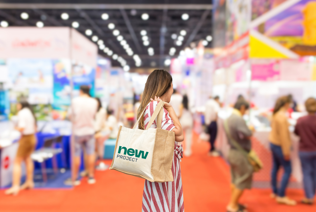 Woman carrying a reusable branded tote bag on her shoulder while walking through a busy trade show exhibition hall