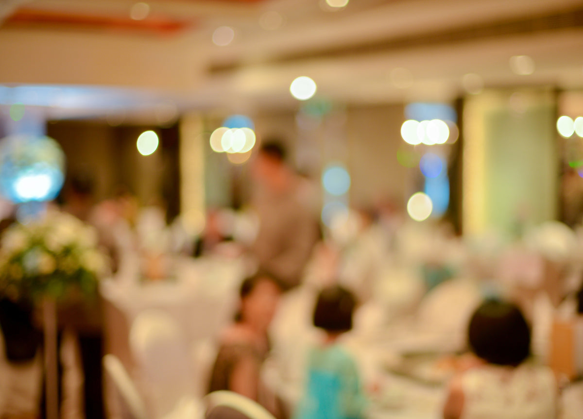 Soft-focus view of a luxurious banquet hall during a company in-house event:  diverse guests in formal attire seated at round white-clothed tables adorned with flowers, under warm chandelier glow and bokeh lights, with a shimmering disco ball adding celebratory ambiance